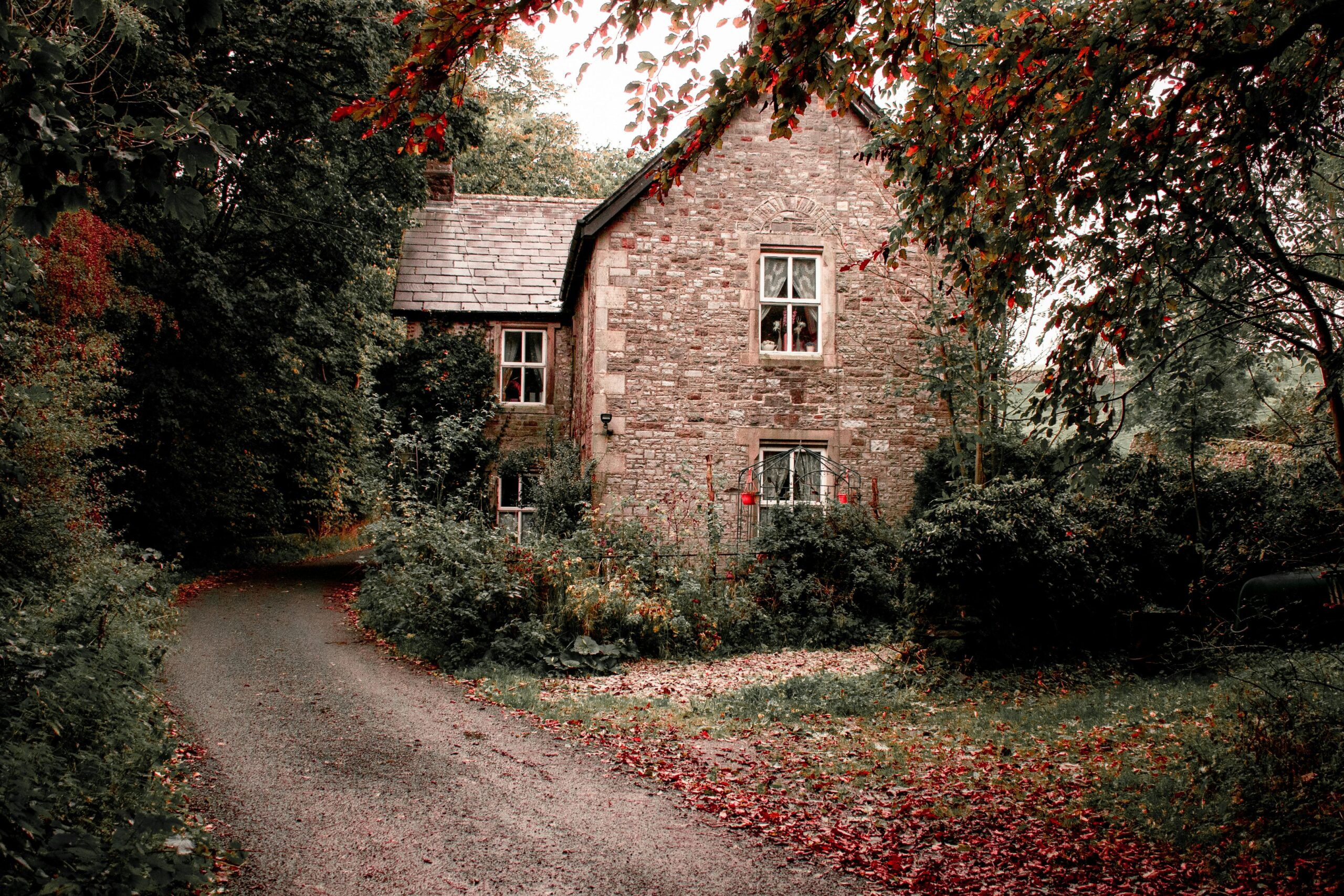A quaint stone cottage surrounded by colorful fall foliage and a winding driveway.